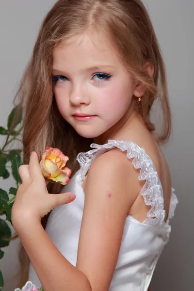 Caucasian girl with beautiful healthy long hairs holding yellow roses with green leaves on a gray background — Stock Photo, Image