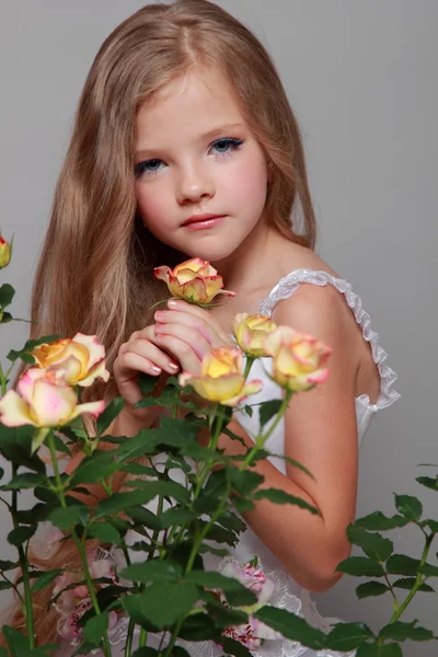 Ragazza caucasica con bei capelli lunghi sani che tengono rose gialle con foglie verdi su uno sfondo grigio — Foto Stock