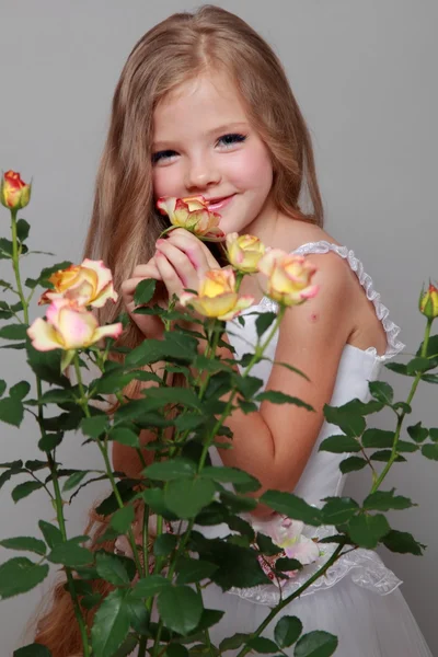 Portrait of a pretty young girl with long hair holds a beautiful yellow rose on a gray background — Stock Photo, Image