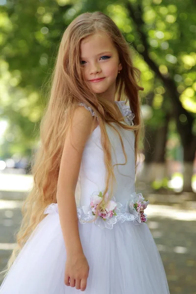 European blonde smiling little girl in a white ball gown in the summer park outdoors — Stock Photo, Image