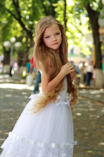 Charming young girl with long healthy hair in a beautiful white dress walking outdoors — Stock Photo, Image