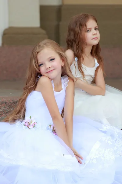 Two young girls in white wedding dresses sitting on the steps outside the building outdoors — Stock Photo, Image