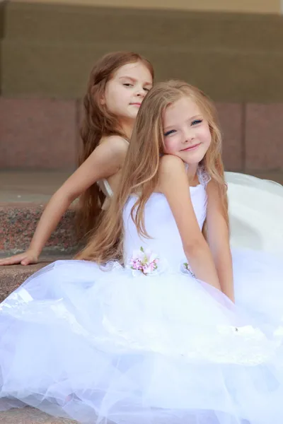 Two young girls in white wedding dresses sitting on the steps outside the building outdoors — Stock Photo, Image