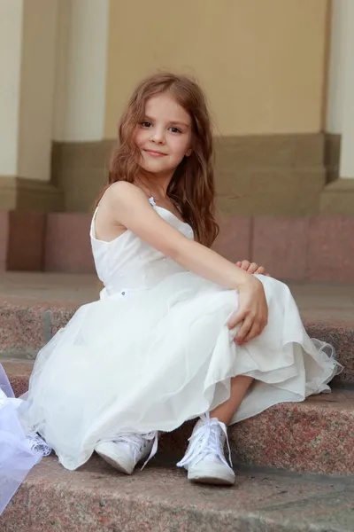 Elegante linda niña en un vestido blanco con hermoso pelo en zapatillas de deporte en la belleza y la moda — Foto de Stock