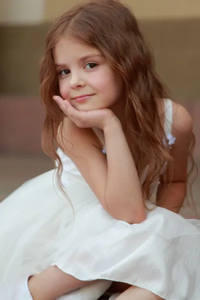 Portrait de mignonne petite fille souriante aux cheveux longs dans une belle robe est assis sur les marches à l'extérieur — Photo