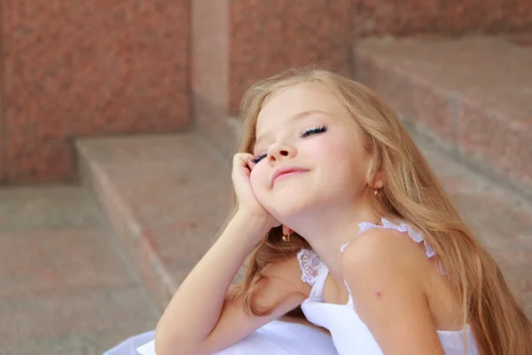 Retrato de linda niña sonriente con el pelo largo en un hermoso vestido está sentado en los pasos al aire libre —  Fotos de Stock