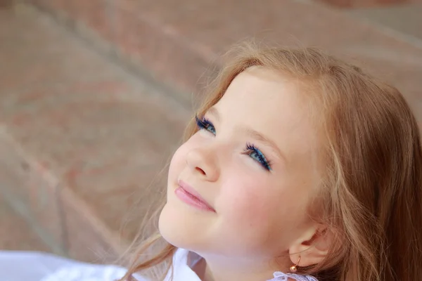 Счастливая улыбающаяся маленькая девочка в белом бальном платье и сидя на лестнице на открытом воздухе — стоковое фото