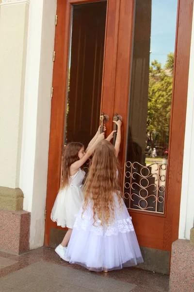 Dva usmívající se holčička v krásné plesové šaty otevřít dveře do budovy venku — Stock fotografie