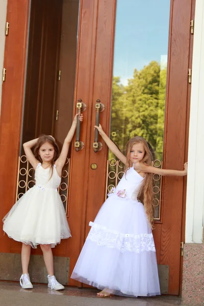 Zwei lächelnde kleine Mädchen in einem wunderschönen Ballkleid öffnen die Türen zum Gebäude im Freien — Stockfoto