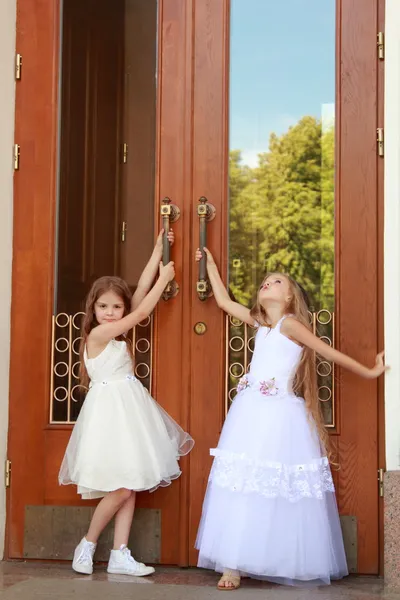 Young girl in white wedding dresses are trying to open the big doors to the building outdoors — Stock Photo, Image