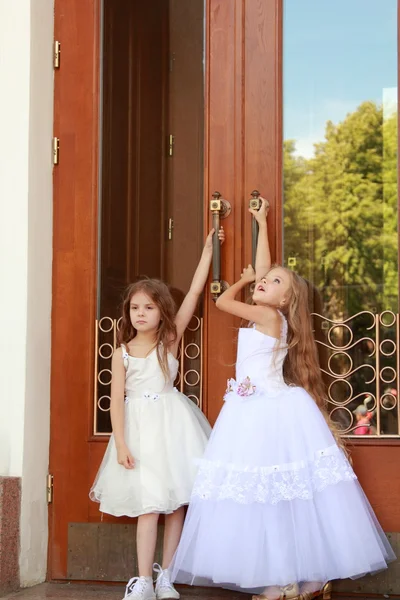 Young girl in white wedding dresses are trying to open the big doors to the building outdoors — Stock Photo, Image