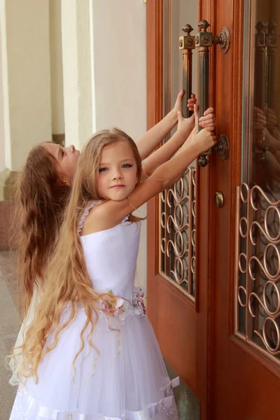Young girl in white wedding dresses are trying to open the big doors to the building outdoors — Stock Photo, Image