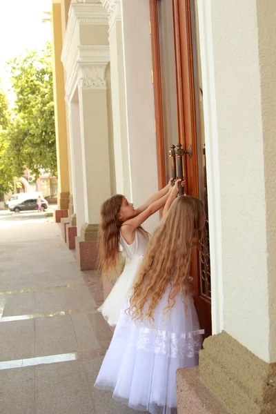 Dos niñas sonrientes en un hermoso vestido de fiesta abren las puertas del edificio al aire libre —  Fotos de Stock