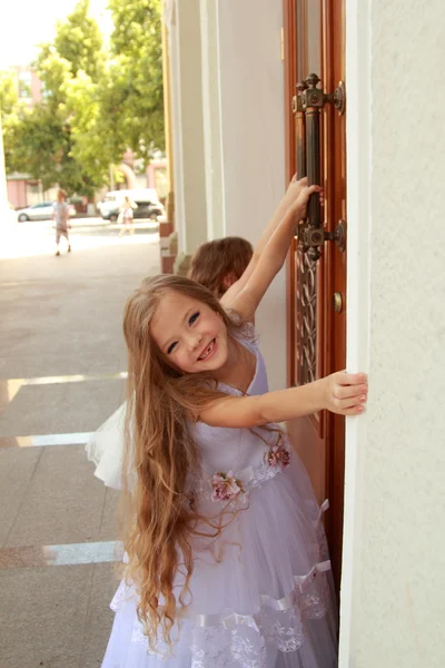 Dwa uśmiechnięta dziewczynka w piękne suknie balowe otworzyć drzwi do budynku na zewnątrz — Zdjęcie stockowe