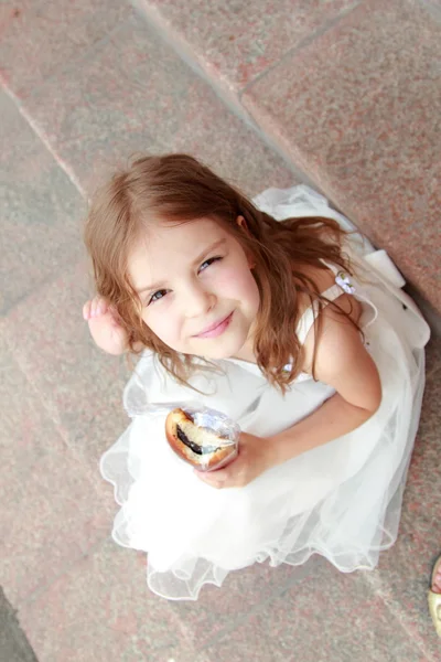 Happy smiling little girl in a white ball gown and sitting on the stairs outdoors — Stock Photo, Image