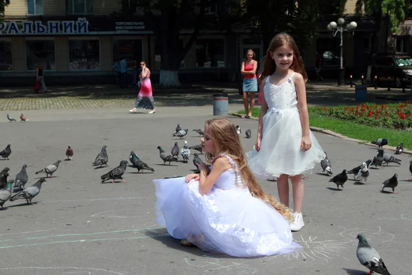 Två små flickor i vita balklänningar mata duvor utomhus — Stockfoto