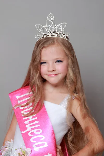 Hermosa niña con el pelo largo y rubio en un vestido de princesa blanca con una cinta roja y la palabra "Princesa del país" en el idioma ucraniano —  Fotos de Stock