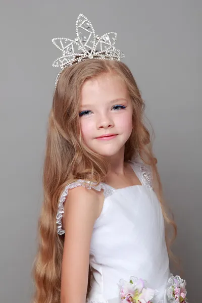 Улыбающаяся маленькая девочка с длинными волосами в короне на сером фоне на празднике — стоковое фото