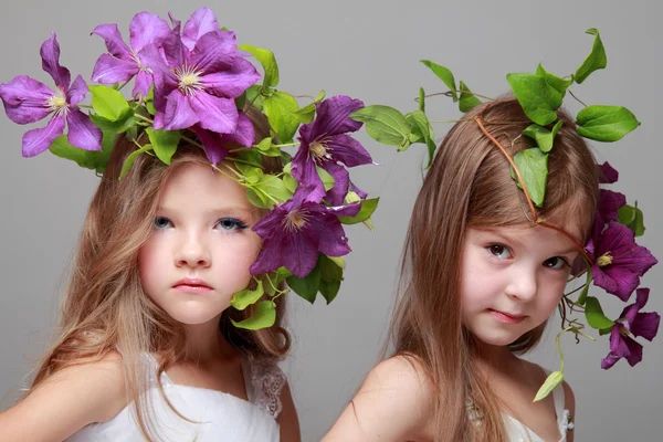 Två vackra små flickor i vita klänningar och frisyrer från färska clematis — Stockfoto