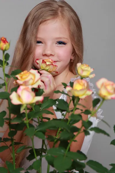 European smiling little girl in a white dress with long hair holds a healthy fresh roses with green leaves on Beauty and Fashion — Stock Photo, Image