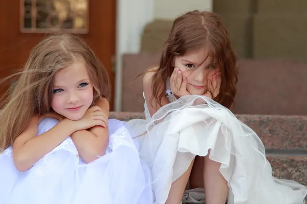 Happy smiling little girl in a white ball gown and sitting on the stairs outdoors — Stock Photo, Image