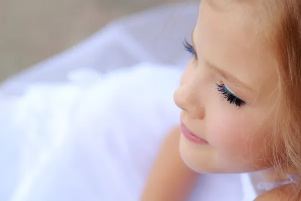 Elegante schattig klein meisje met make-up in een witte jurk met mooie haren — Stockfoto