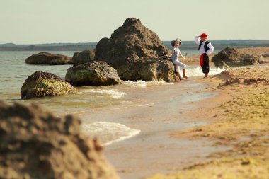 Deniz kıyısında mutlu neşeli sevimli erkek ve kız korsan kostümleri yalınayak koşmak
