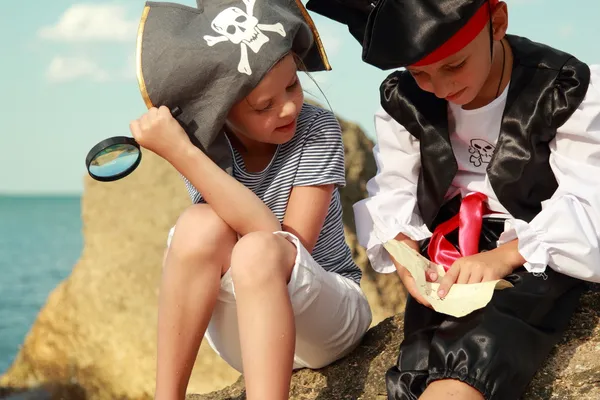 Niño y niña en un traje de pirata con un mapa y una lupa — Foto de Stock