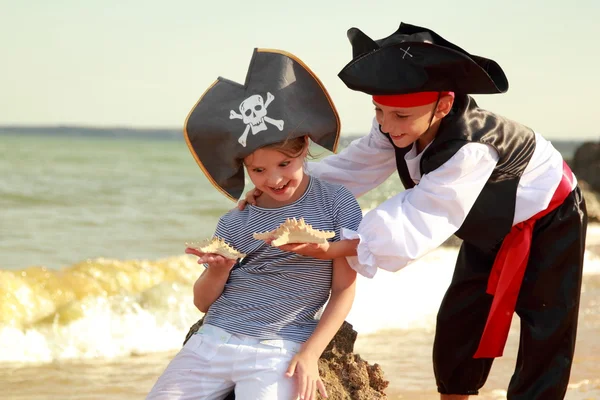 Menino bonito em um traje de pirata e uma menina em um chapéu com um símbolo de esqueleto de pirataria — Fotografia de Stock