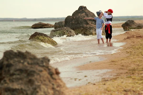 Fröhlich fröhlich süße Jungen und Mädchen in Piratenkostümen barfuß entlang der Meeresküste laufen — Stockfoto