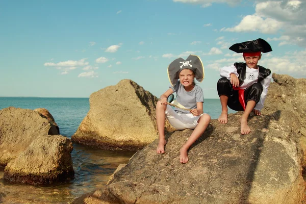 Alegre niña y niño en traje de fantasía pirata sentado en la orilla del mar — Foto de Stock