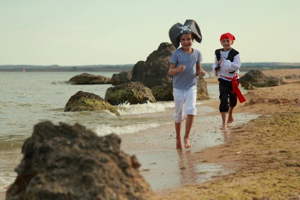 Wesoły zadowolony ładny chłopiec i dziewczyna w stroju pirata boso biegać wzdłuż wybrzeża Morza — Zdjęcie stockowe