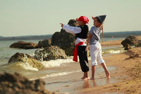 Cheerful happy cute boy and girl in pirate costumes barefoot run along the sea coast — Stock Photo, Image