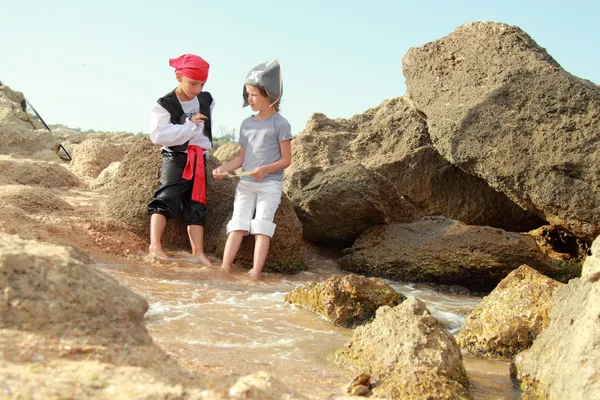 Joyful menina e menino em fantasia vestido pirata sentado na costa do mar — Fotografia de Stock