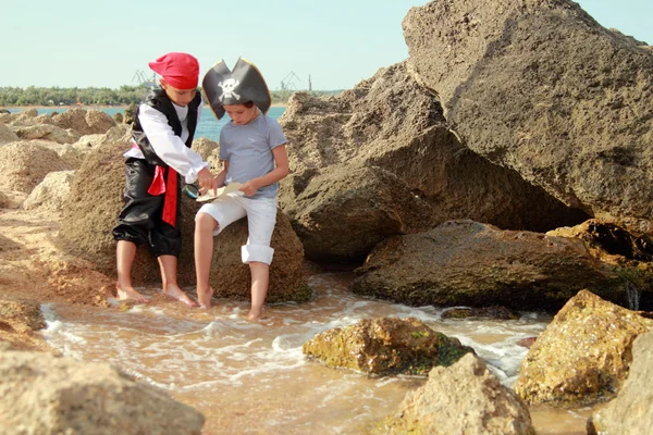 Радісна маленька дівчинка і хлопчик у вишуканій сукні пірат сидить на березі моря — стокове фото
