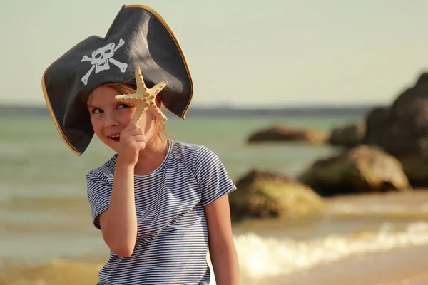 Menina bonito em um chapéu com um crânio símbolo pirataria detém uma estrela do mar — Fotografia de Stock
