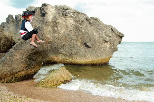 Angry little boy dressed as a pirate is sitting on a large rock in the sea — Stock Photo, Image