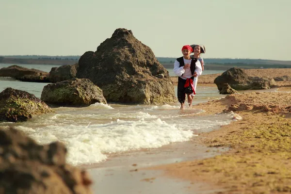 Cheerful happy cute boy and girl in pirate costumes barefoot run along the sea coast — Stock Photo, Image