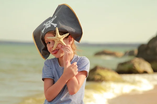 Carino bambina in un cappello con un teschio simbolo di pirateria tiene una stella marina — Foto Stock