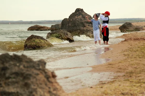 Fröhlich fröhlich süße Jungen und Mädchen in Piratenkostümen barfuß entlang der Meeresküste laufen — Stockfoto