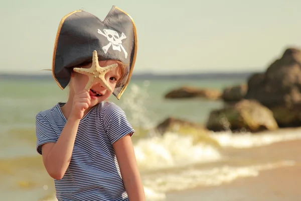 Menina bonita em chapéu de pirata com um crânio segurando uma estrela do mar na praia — Fotografia de Stock