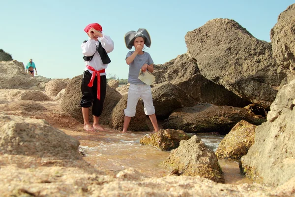 Joyful menina e menino em fantasia vestido pirata sentado na costa do mar — Fotografia de Stock