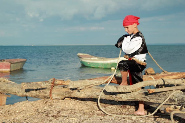 Charming young pirate boy in a red bandanna standing against the background of blue sea — Stock Photo, Image