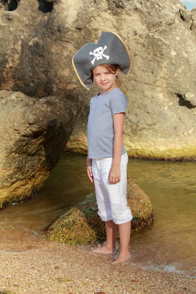 Charming young girl in a pirate hat standing in water at the beach in summer — Stock Photo, Image