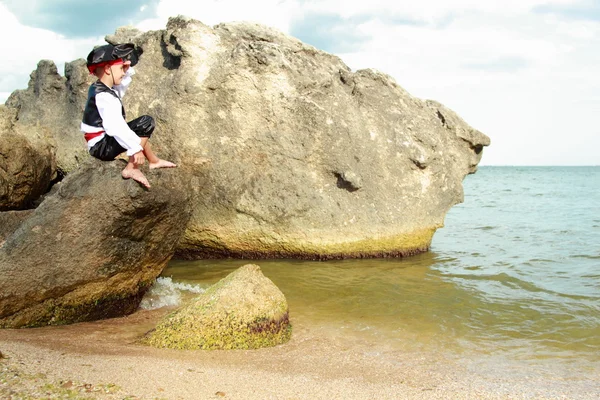 Mérges kis fiú öltözött, mint egy kalóz ül egy nagy szikla a tengerbe — Stock Fotó