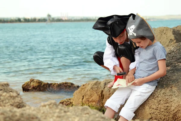 Hermosos niños pequeños pirata niño y niña sosteniendo un mapa pirata y una lupa —  Fotos de Stock