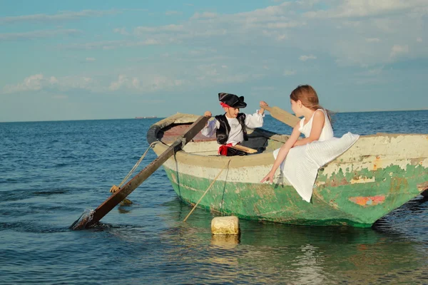 Mooie lachende jonge jongen en meisje als een piraat en een dame in de oude kleine boot in de open zee zwemmen — Stockfoto