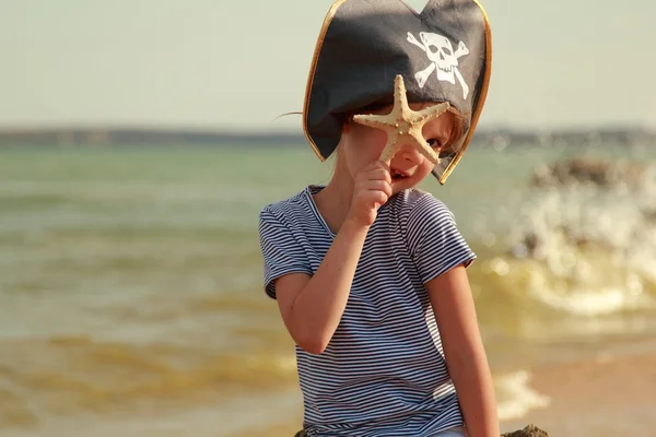 Caucasian sweet young girl in a pirate hat with a starfish on a background of a sea landscape — Stock Photo, Image