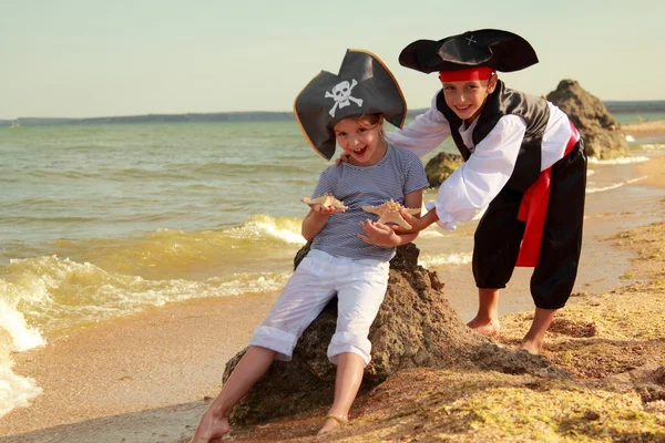 Hermoso niño y niña vestidos con trajes de pirata y la celebración de estrellas de mar en la playa —  Fotos de Stock