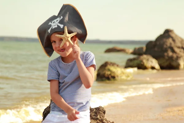 Menina bonita em chapéu de pirata com um crânio segurando uma estrela do mar na praia — Fotografia de Stock